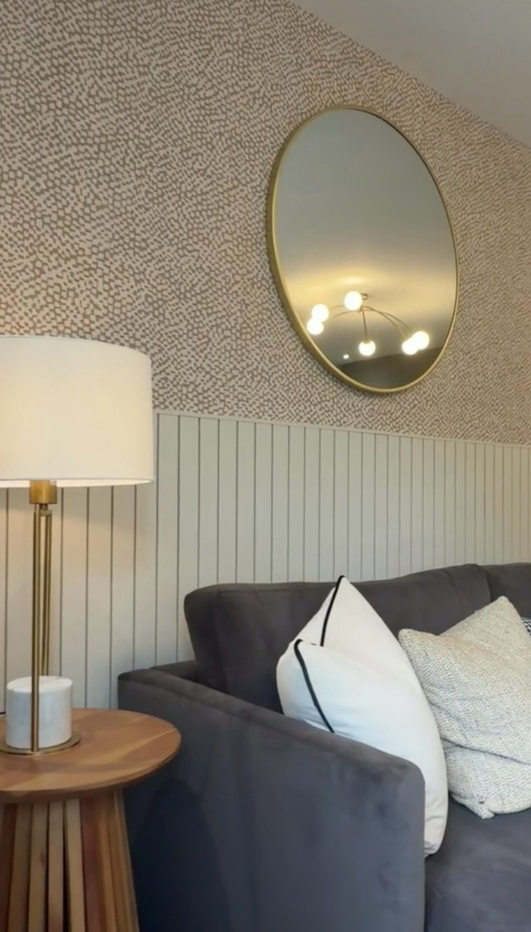 Gold round mirror above a grey sofa and brass lamp